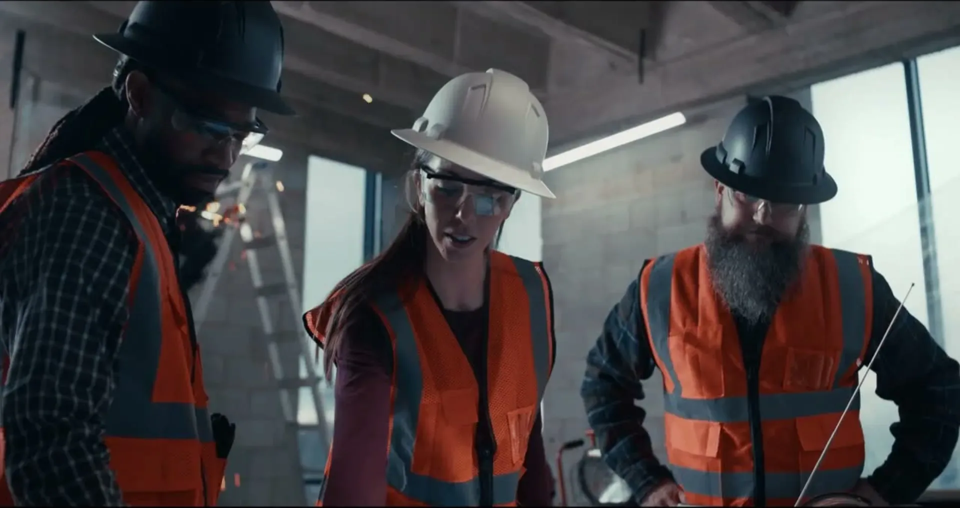 Three crew members in hard hats and safety glasses look down at the plans table