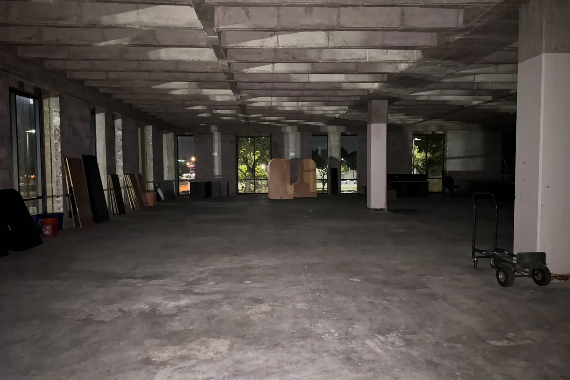 Location scout photo: a dark office floor stripped to bare concrete, with columns, a coffered ceiling and windows along one wall