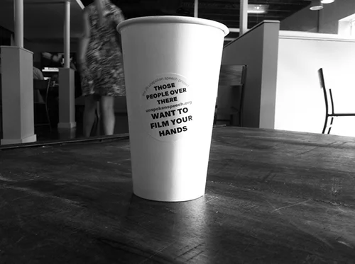On set for The Unspoken Speech Project: a coffee cup stickered "Those people over there want to film your hands"