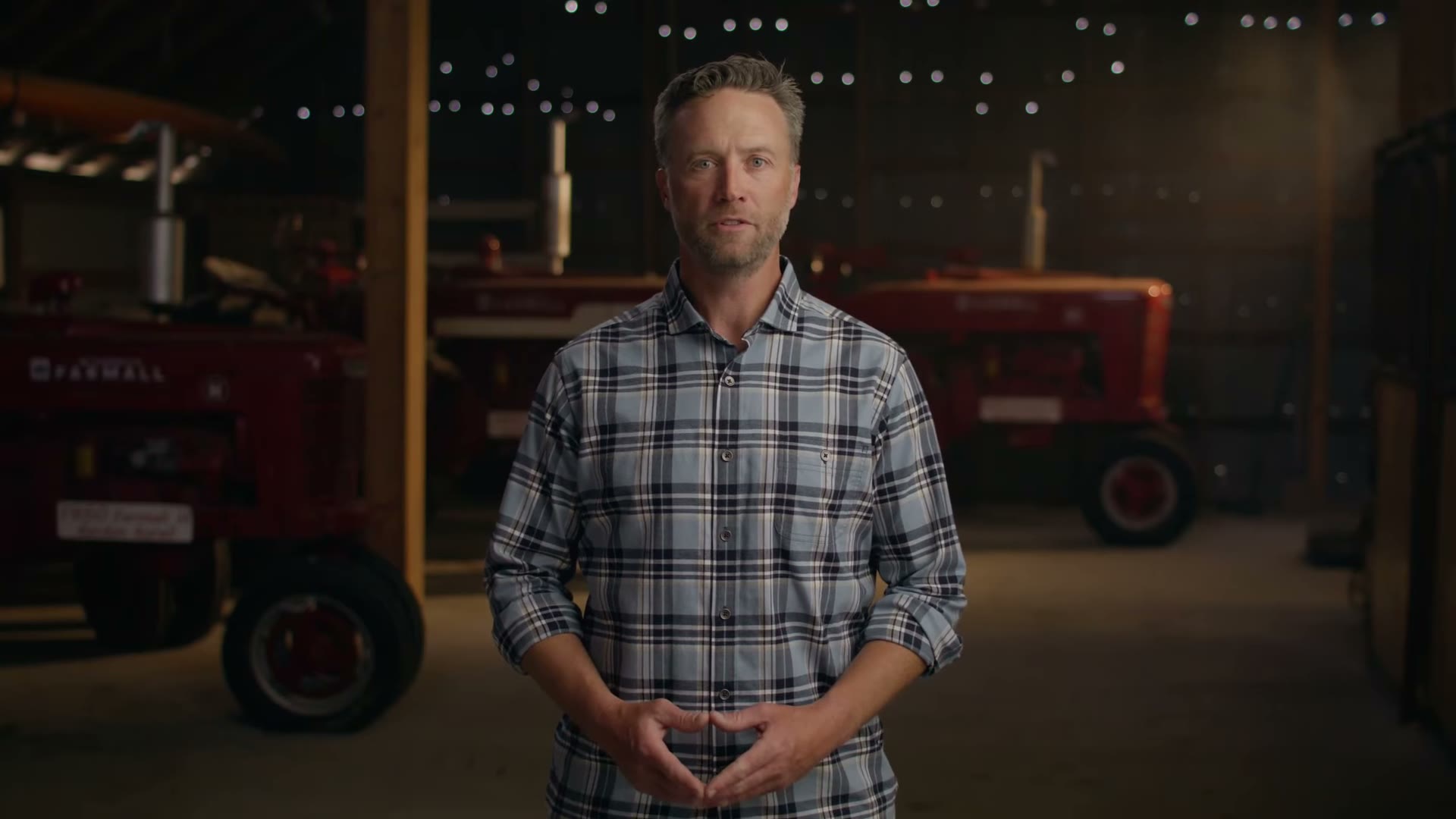 Lincoln Hough speaking to camera in a barn of vintage tractors