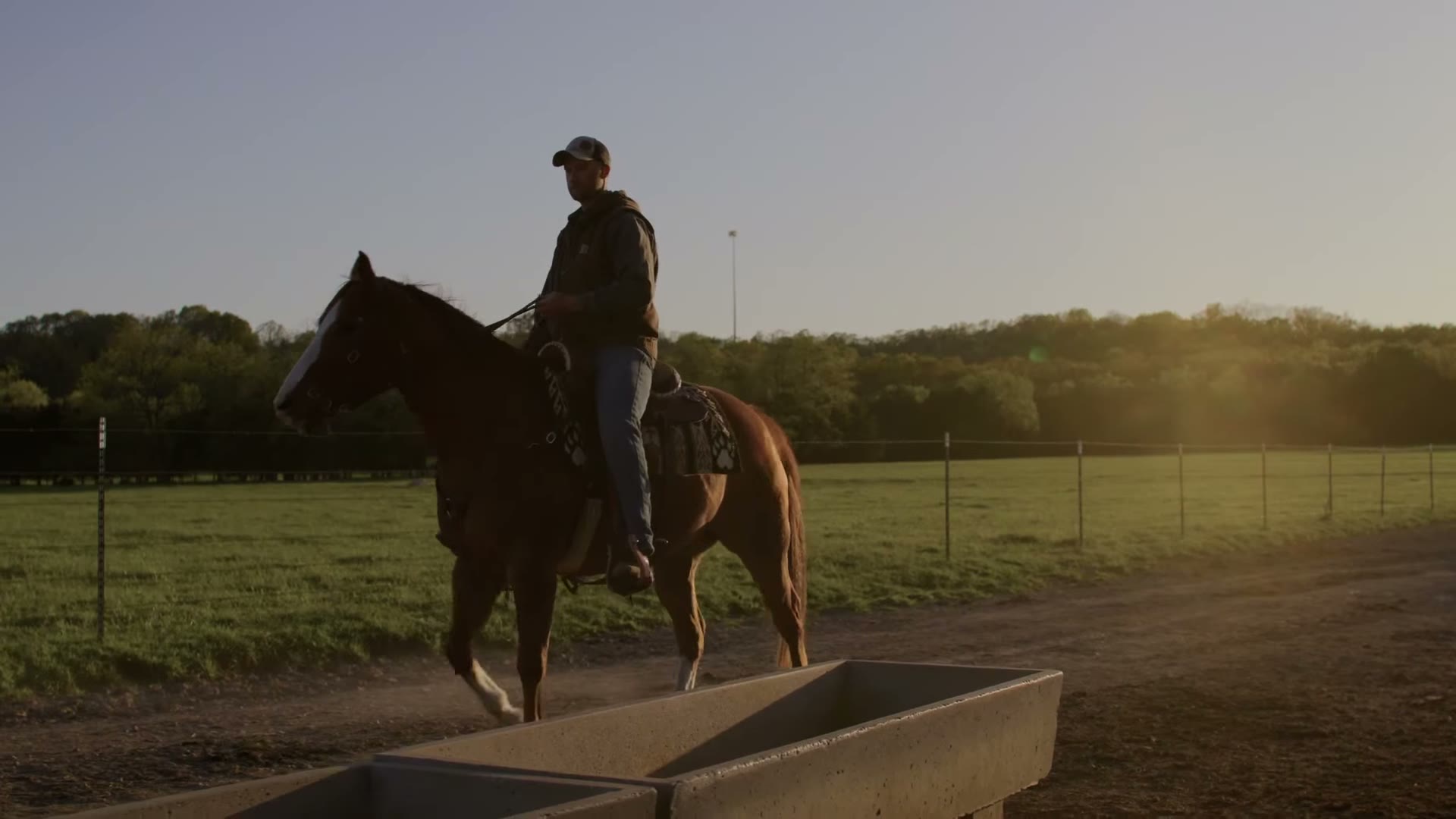 A rider on horseback crossing a Missouri farm at golden hour