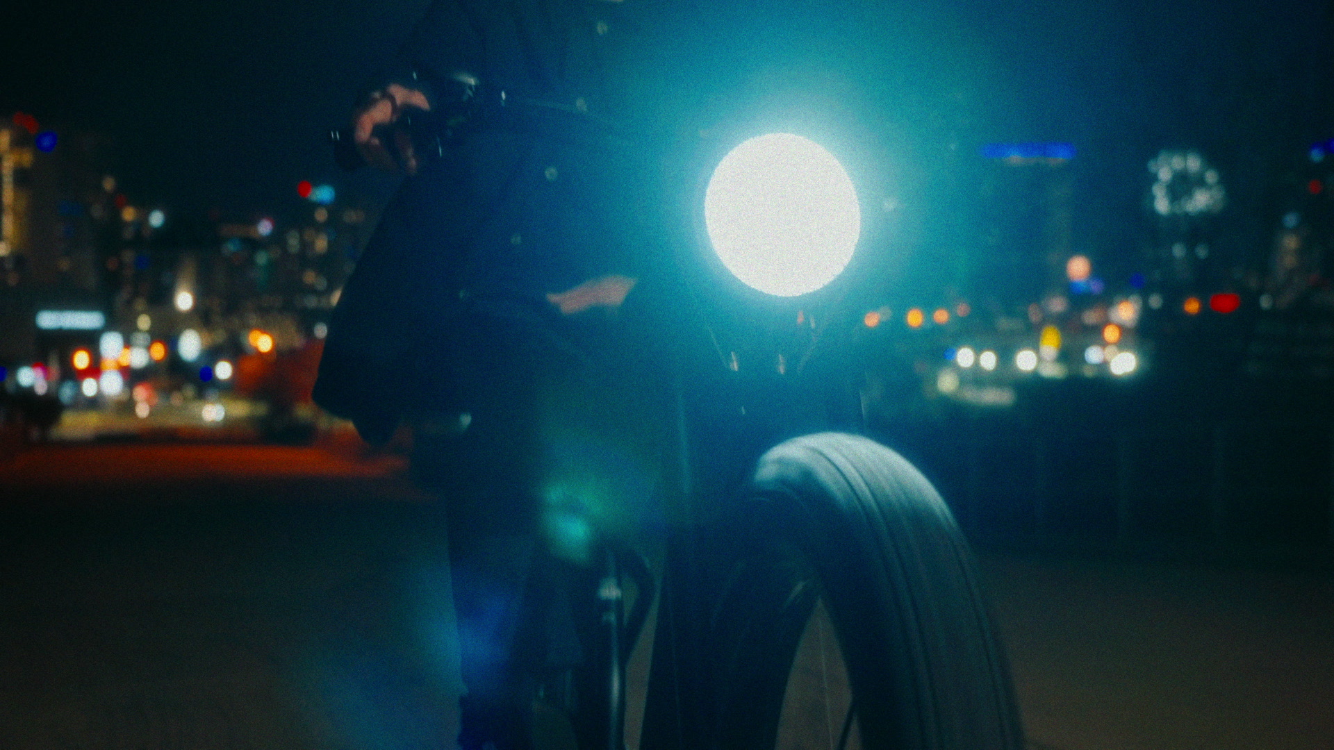 Night bike portrait with oversized headlight flare, city bokeh, and rider silhouette.