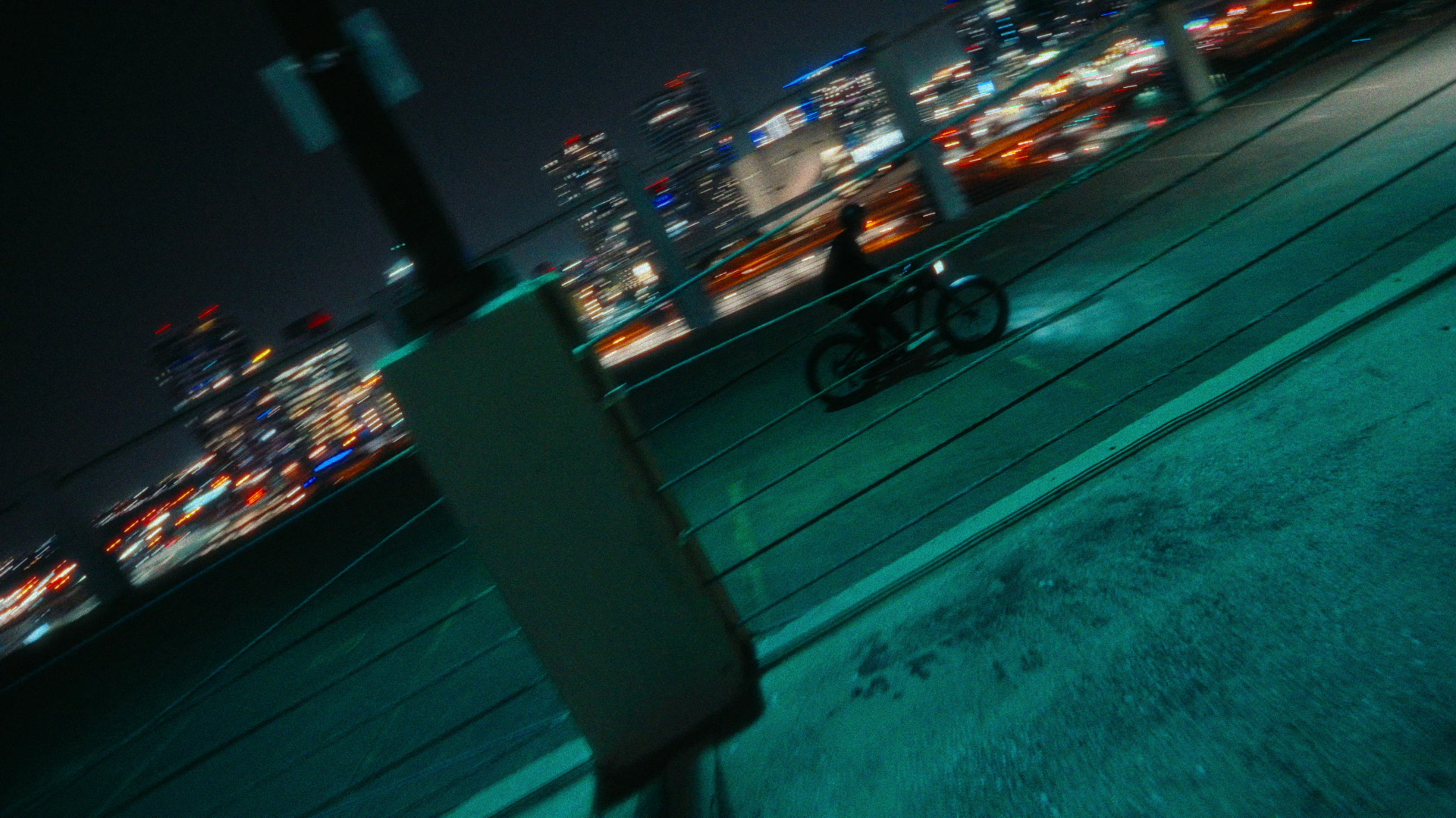 Rooftop bike silhouette against a blurred downtown skyline and teal city glow.