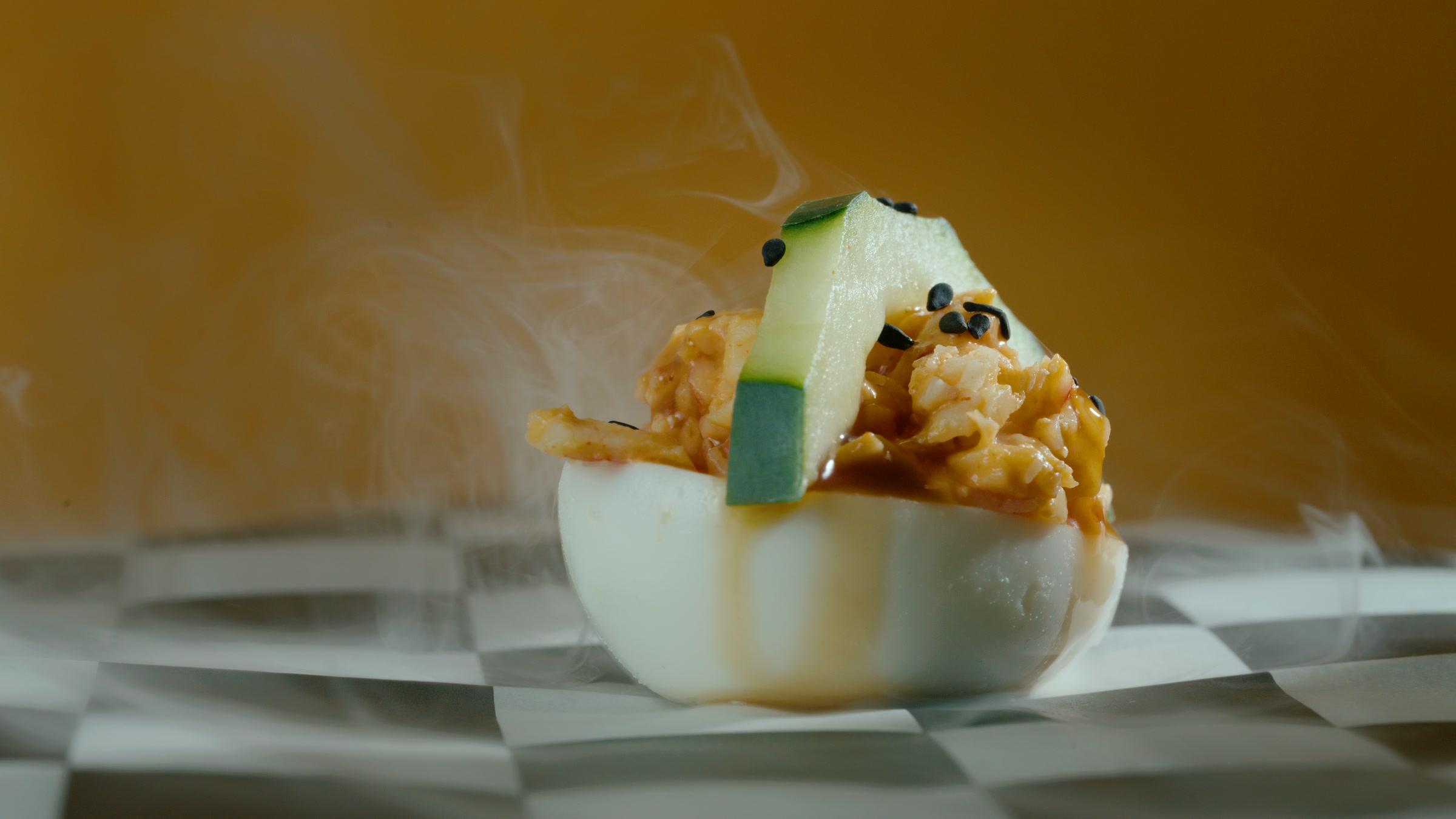 Cucumber topped deviled egg hero with visible smoke and fresh green garnish.