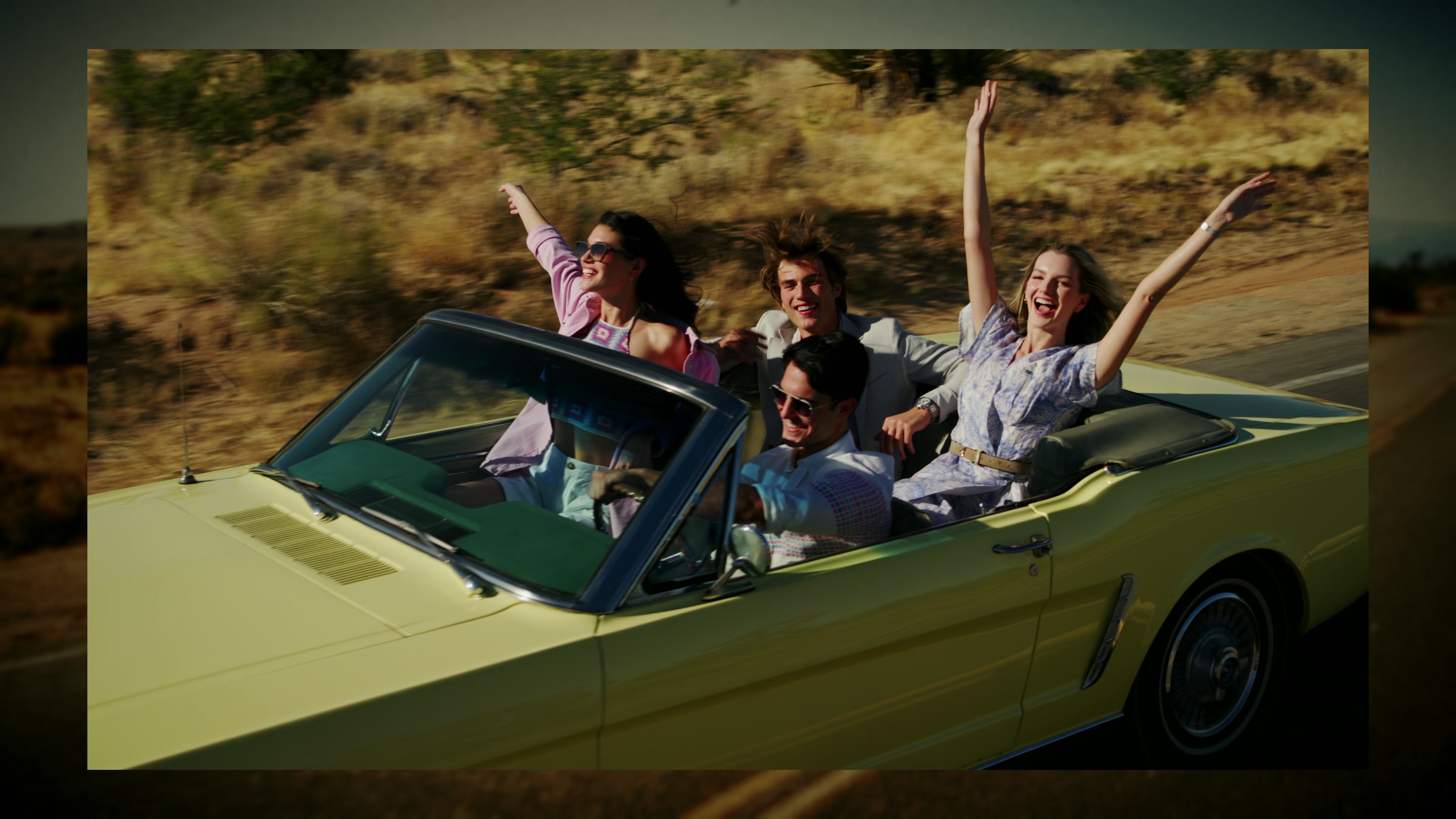 Group celebration around the yellow convertible in a sunlit desert setting.