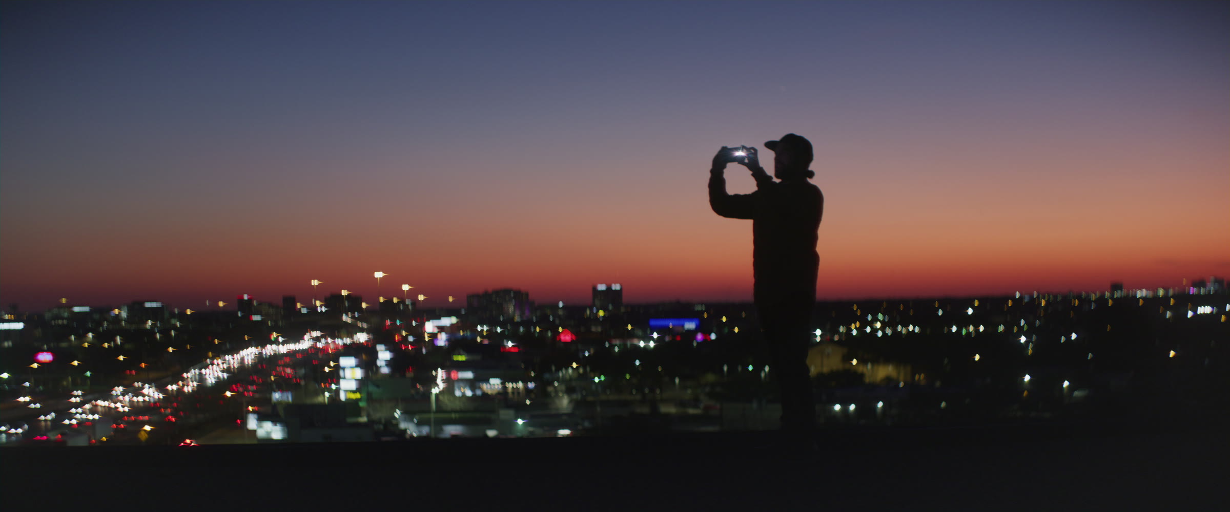 Rooftop silhouette holding a phone against a city skyline at blue hour.