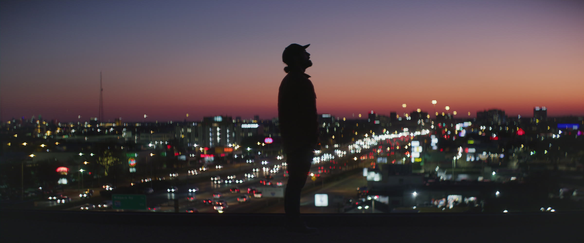 Profile silhouette over a sunset city skyline with warm horizon color and night traffic.