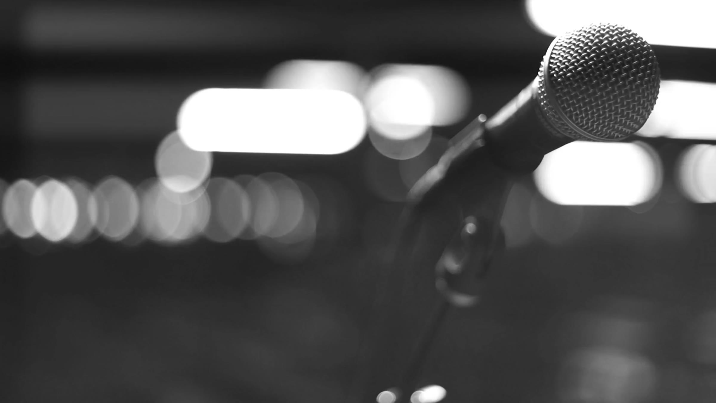 Black and white microphone frame with soft stage bokeh and shallow depth of field.