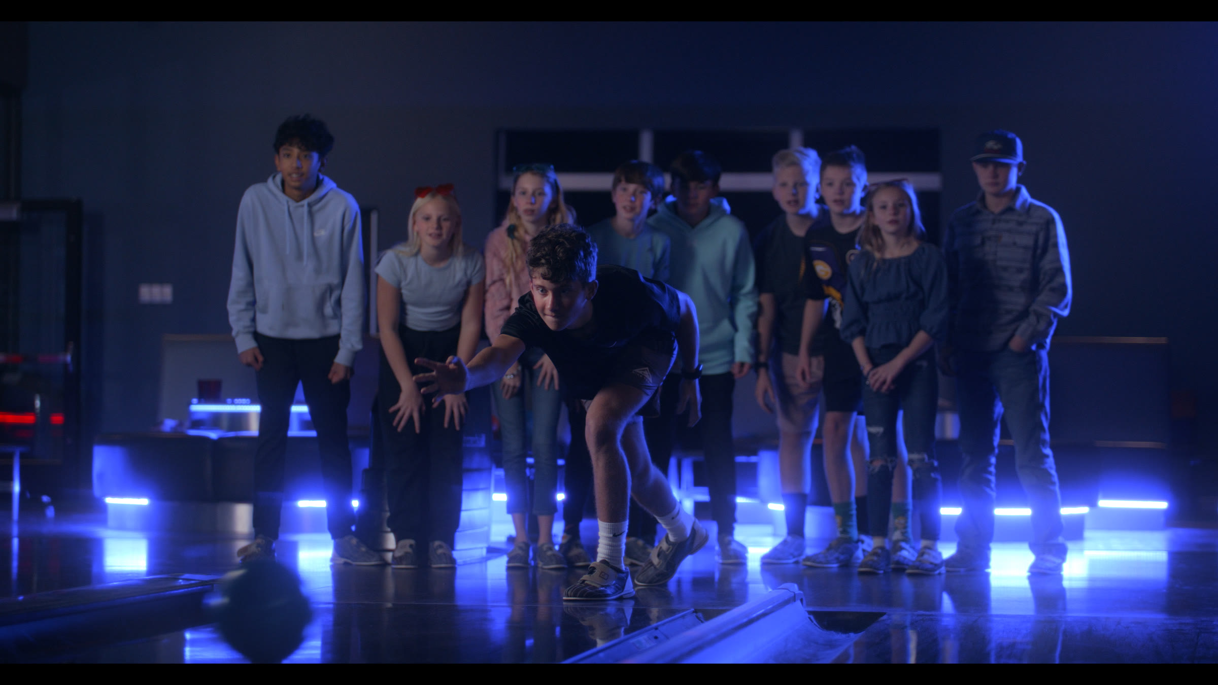 Wide group frame in blue practical light with kids gathered on a polished floor.