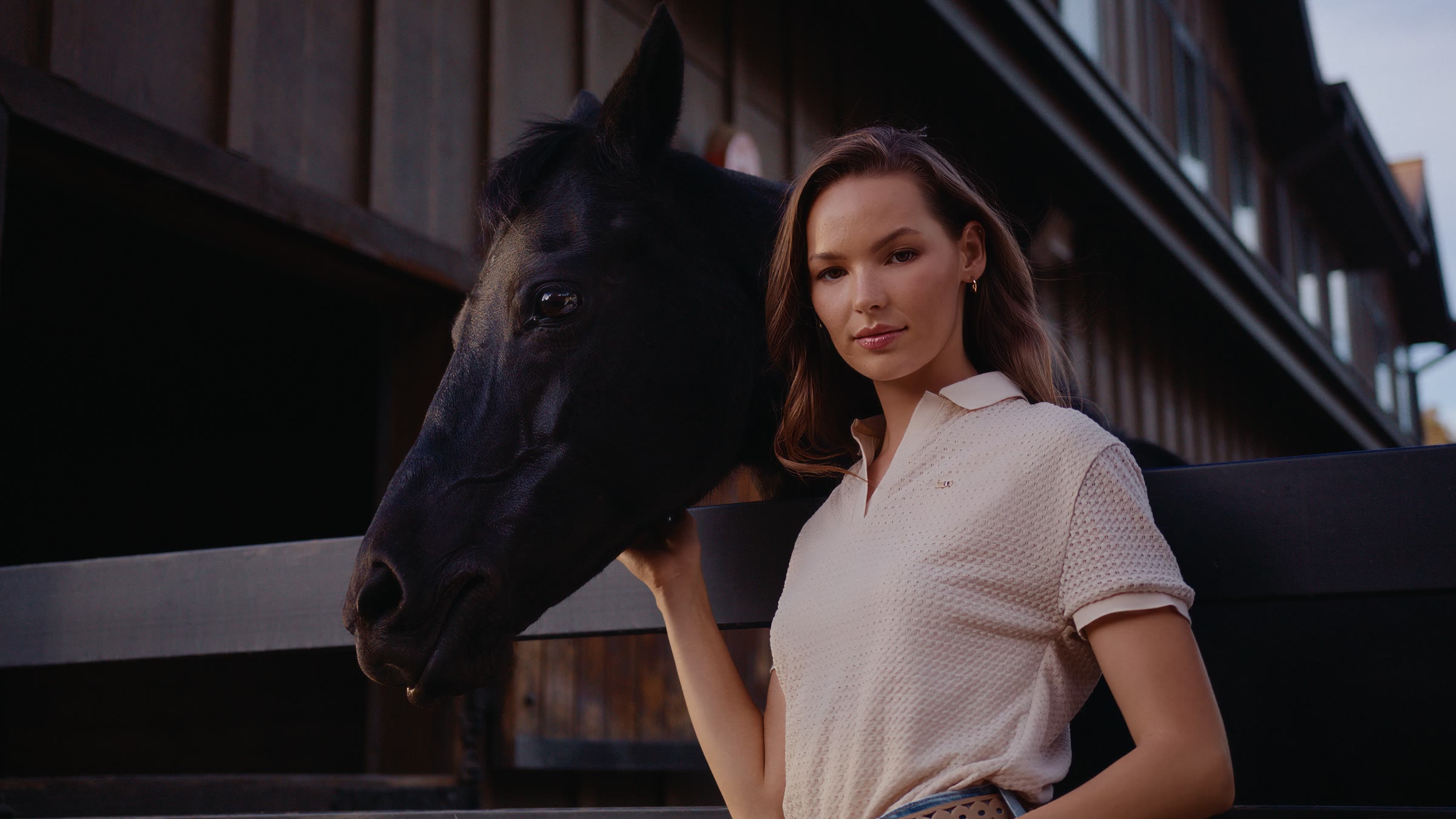 Barn-side horse portrait with model in white polo and quiet stable light.