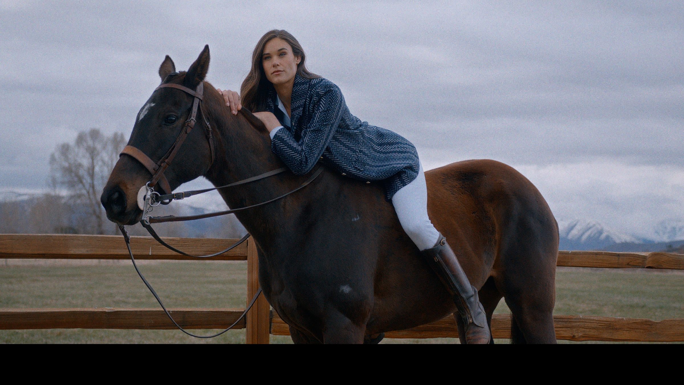 Utah ranch frame with model on horseback, overcast sky, and mountain backdrop.