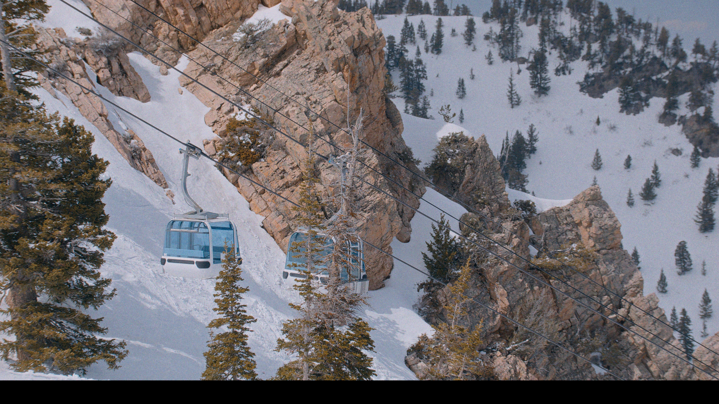 Snowy Utah gondola ridge frame with rock face, ski lift, and alpine scale.
