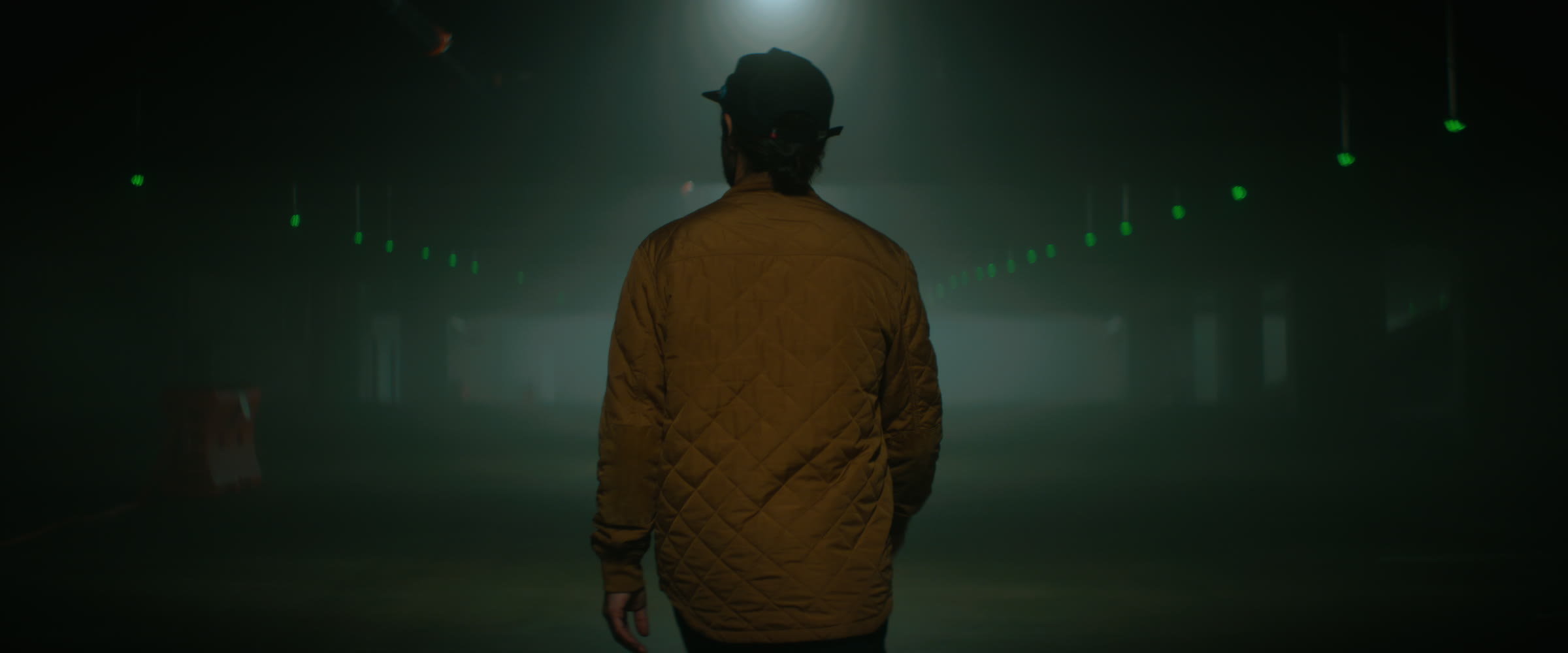 Anamorphic downtown fog frame with a figure walking into green tunnel light.