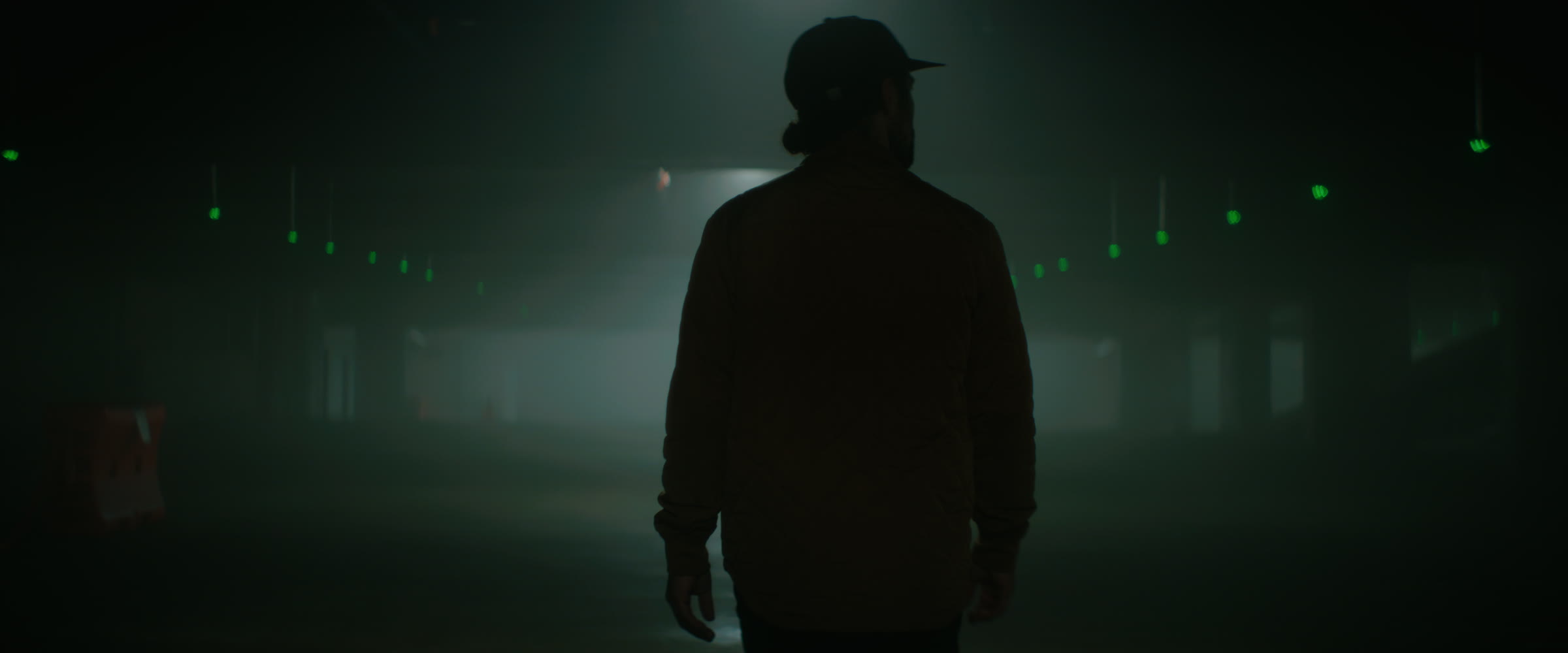 Dark silhouette in downtown fog with green practical lights receding into tunnel depth.