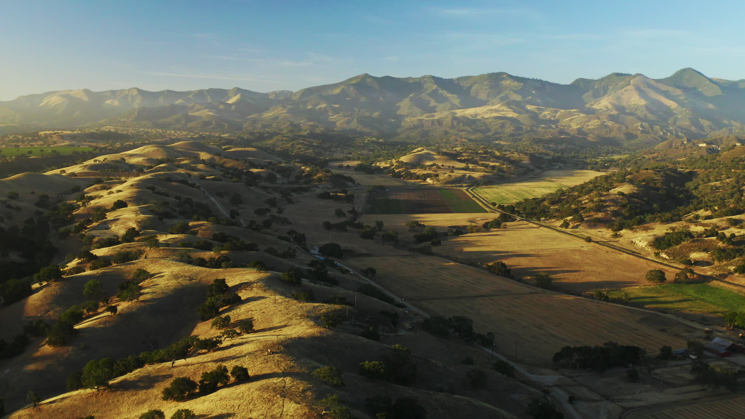 Aerial ridge landscape with rolling hills, oak trees, and golden valley light.